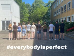 Schüler*innen stehen mit dem Rücken zur Kamera in einer Reihe, darunter #EveryBodyIsPerfect